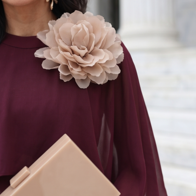 Mulher com vestido bordô com flor bege e clutch bege segura em fundo claro