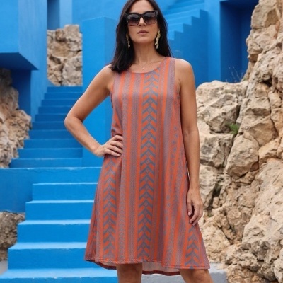 Vestido laranja e cinza com padrão geométrico, sem mangas, mulher de óculos em escadaria azul