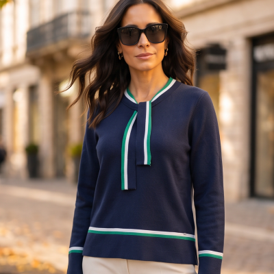 Camisola de malha azul escuro com riscas verdes e brancas e laço no decote, usada com calças claras e óculos escuros