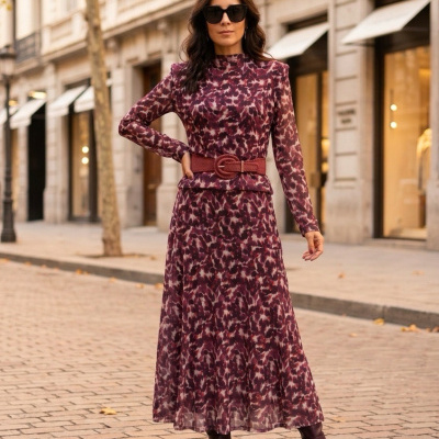 Mulher com vestido estampado em tons vinho e botas castanhas numa rua com folhas de outono.