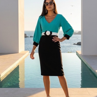 Mulher com vestido azul e preto, cinto branco com flor, sapatos dourados e óculos de sol junto a piscina e mar