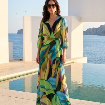 Mulher com vestido longo colorido e óculos de sol junto a uma piscina e vista para o mar.