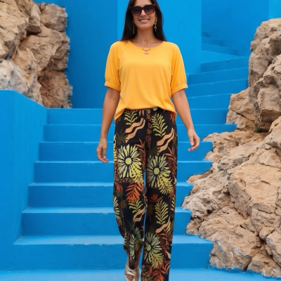 Mulher com blusa amarela e calças florais em escadas azuis perto de rochas