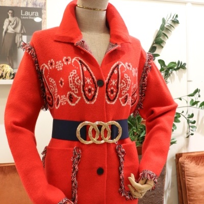 Casaco vermelho de malha com padrão étnico e cinto azul escuro com fivela dourada em manequim.