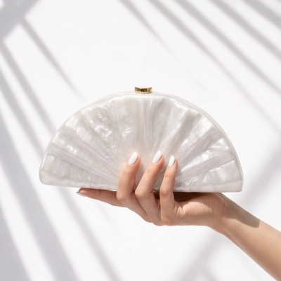 Carteira clutch branca pérola semicircular com textura marmorizada segura por mão feminina