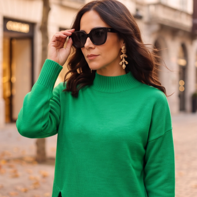 Mulher com casaco verde, óculos de sol pretos e brincos dourados numa rua urbana
