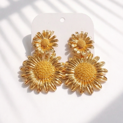 Brincos dourados em forma de flor sobre cartão branco