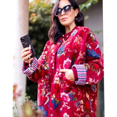 Casaco vermelho com padrão floral e detalhes às riscas nas mangas usado por mulher com óculos e segurando telemóvel preto