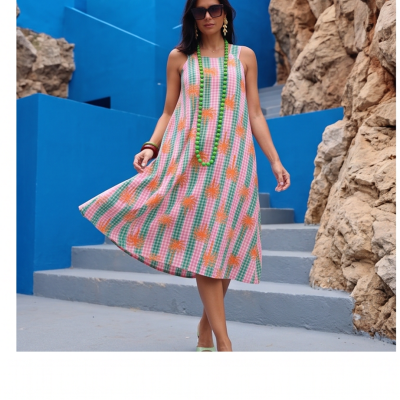 Vestido midi xadrez verde com flores laranja usado com colar verde e óculos em cenário azul