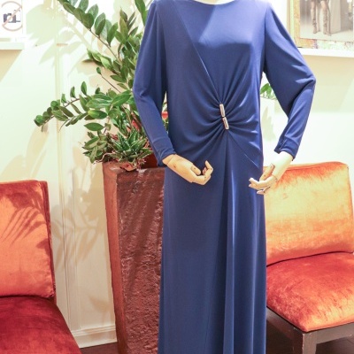 Vestido comprido azul escuro com detalhe franzido na cintura, exposto em manequim entre cadeiras laranja.