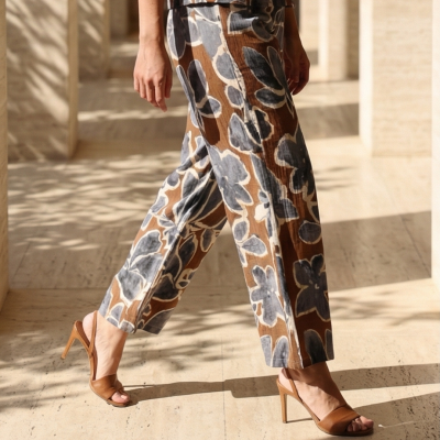 Calças compridas com padrão floral castanho e cinza com sandálias castanhas em piso claro