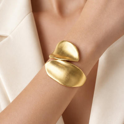 Pulseira dourada assimétrica em pulso com roupa bege clara