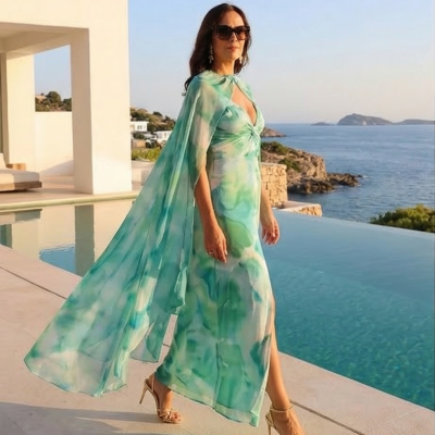 Mulher com vestido longo verde e azul com capa, sandálias de salto, junto a piscina e mar