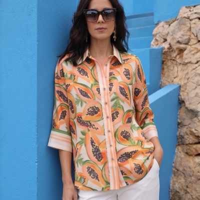 Camisa feminina com padrão de papaia e calças brancas com parede azul ao fundo