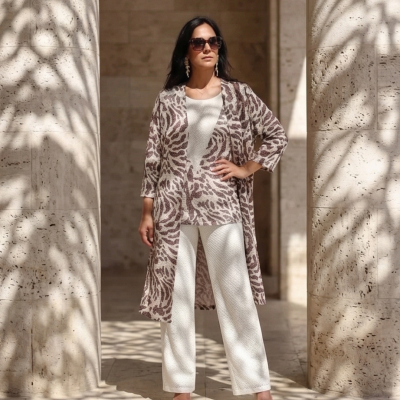 Mulher de casaco comprido estampado, conjunto branco e óculos escuros, em espaço com colunas de pedra