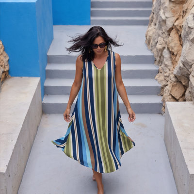 Vestido feminino listrado azul, verde e castanho em mulher a caminhar numa escada cinzenta entre paredes azuis e rochosas.