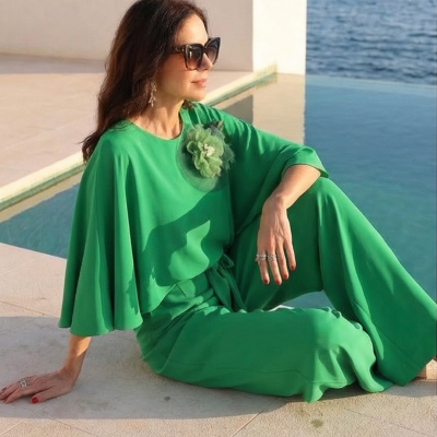 Macacão verde com detalhe de flor, mulher sentada ao lado de piscina e mar.