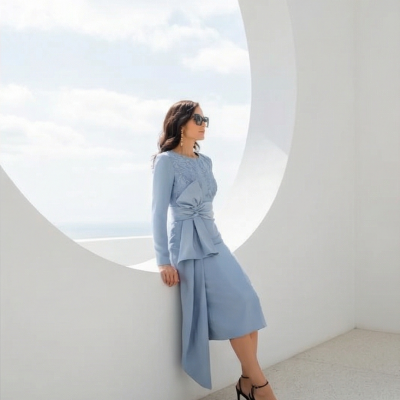 Mulher com vestido midi azul claro e sandálias pretas de salto alto junto a parede branca com buraco circular