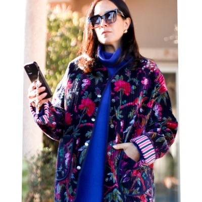 Mulher com casaco acolchoado floral, camisola azul e calças de ganga a segurar telemóvel preto