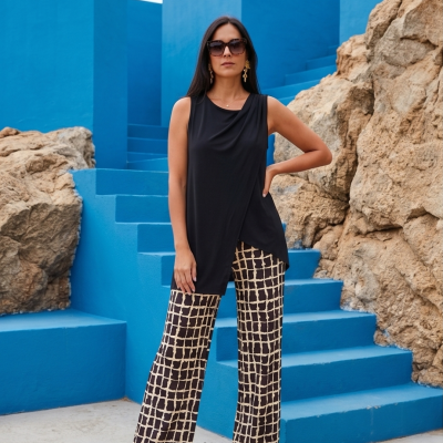 Mulher de top preto e calças xadrez bege e preto, com sandálias pretas, óculos de sol e brincos, em escadaria e paredes azuis.