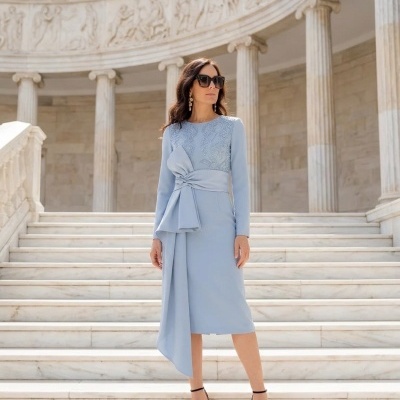 Mulher com vestido azul claro e óculos escuros numa escadaria de pedra branca com colunas clássicas