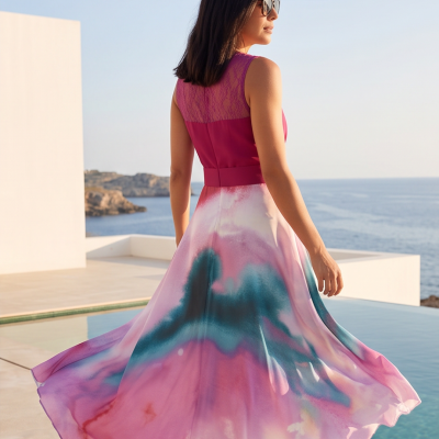 Mulher a usar vestido cor de rosa com renda e padrão colorido junto a piscina com mar ao fundo