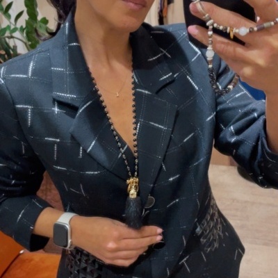 Fato feminino escuro com padrão riscado branco e tachas, em selfie com smartphone em mão.