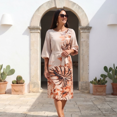 Mulher a usar vestido floral bege com cinto e sandálias planas num espaço exterior com parede branca e cactos em vasos.
