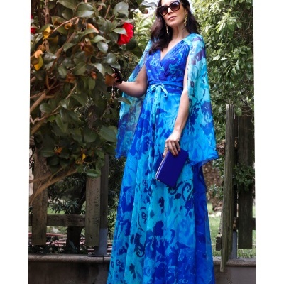 Mulher com vestido longo azul floral e acessórios em ambiente exterior