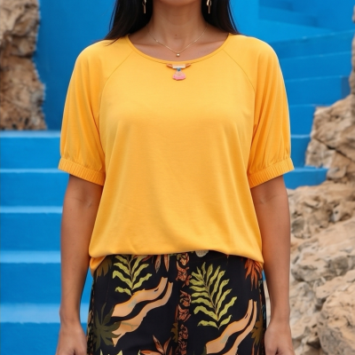 Mulher com t-shirt amarela e calças pretas com padrão floral, escadas azuis e rochas no fundo