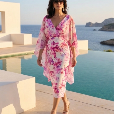 Mulher com vestido midi floral rosa e lilás junto a piscina e mar.