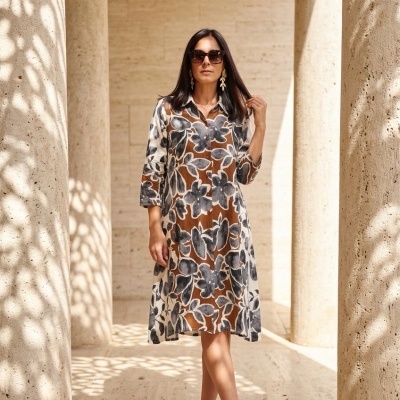 Mulher com vestido midi floral castanho, preto e branco, sandálias pretas e óculos de sol, entre colunas de pedra clara.