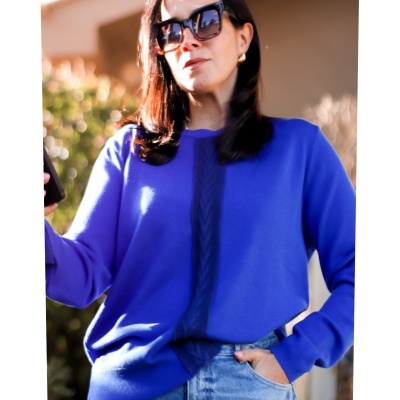 Mulher com camisola azul e jeans azuis claros a usar óculos de sol negros grandes