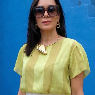 Blusa verde-limão de tecido translúcido com riscas verticais e acessórios dourados