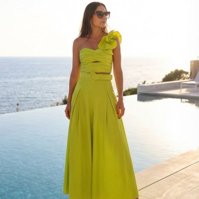 Mulher vestindo vestido longo amarelo esverdeado com alça e cinto, ao lado de piscina e mar ao fundo