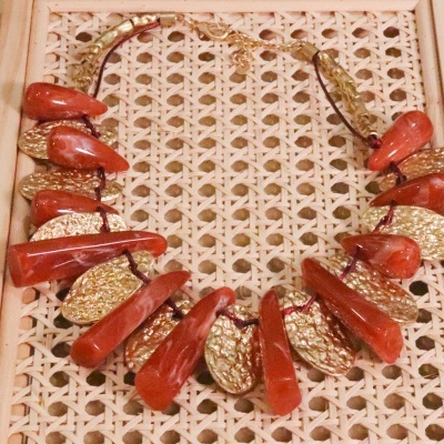 Colar com contas vermelhas e elementos dourados sobre fundo trançado de madeira