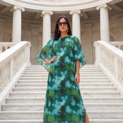 Vestido comprido verde azul com padrão abstrato em escadaria de mármore branco e colunas clássicas