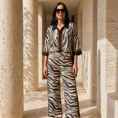 Mulher com roupas estampadas em padrão tipo zebra e sandálias pretas em ambiente com colunas de pedra.