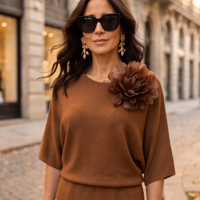Mulher de óculos de sol e camisola castanha com flor decorativa