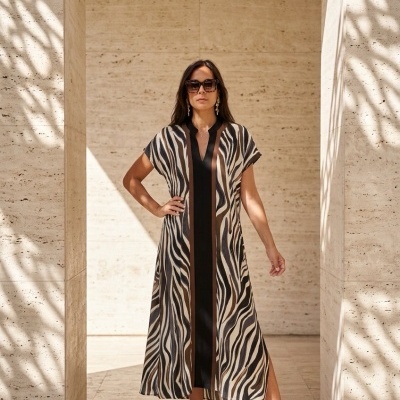Vestido comprido com padrão zebrano em tons bege, preto e castanho usado por mulher com óculos de sol