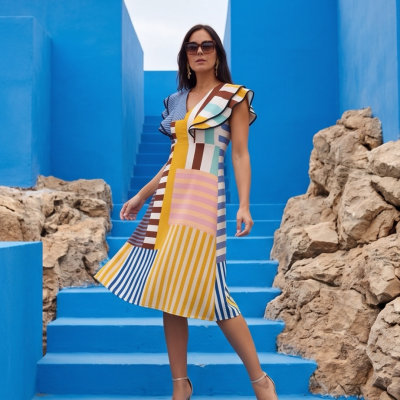 Mulher com vestido midi colorido e sandálias de salto alto em escadaria azul
