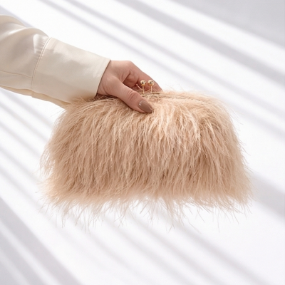 Mala pequena bege de penas com fecho dourado segurada por mão feminina