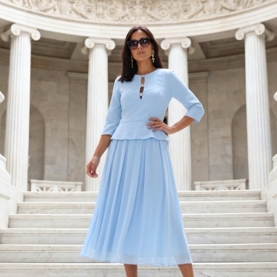 Mulher com vestido azul claro plissado em escadaria de mármore com colunas