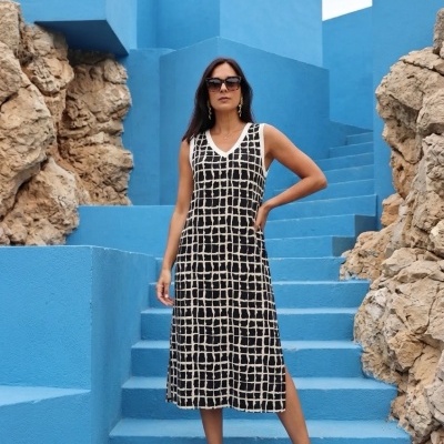 Mulher com vestido midi preto e branco, sandálias pretas, óculos de sol, a posar nas escadas azuis entre rochas.