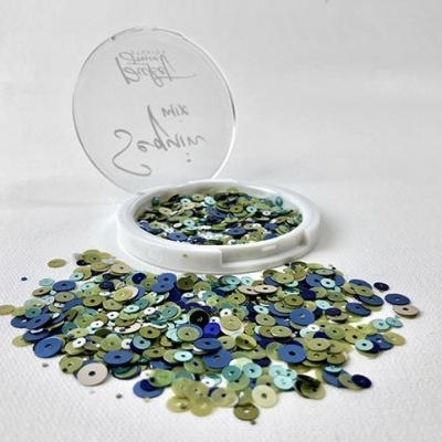 Lantejoulas coloridas em pote transparente aberto sobre superfície branca