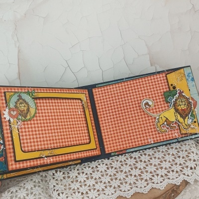 Álbum de scrapbook aberto com padrão xadrez laranja e branco e decorações de leão e renda