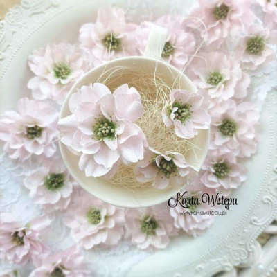 Flores artificiais rosa claro com centros verdes em chávena branca sobre fundo decorativo branco