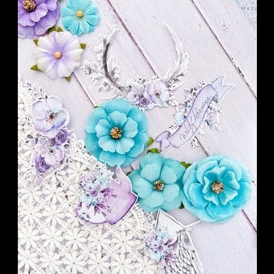 Flores artificiais azul e lilás com detalhes dourados e elementos decorativos sobre madeira branca