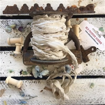 Fita de tecido bege enrolada numa estrutura metálica enferrujada com carretéis de madeira e etiqueta Old Fashion Ribbons