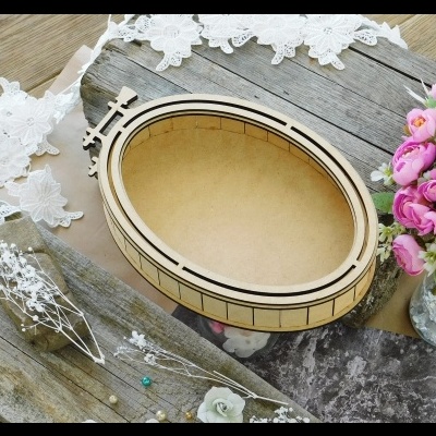 Caixa de madeira oval com borda preta, flores artificiais e renda sobre mesa de madeira